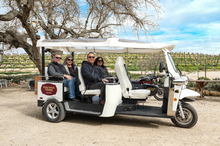 Four people seated in a small tour vehicle in a vineyard setting.