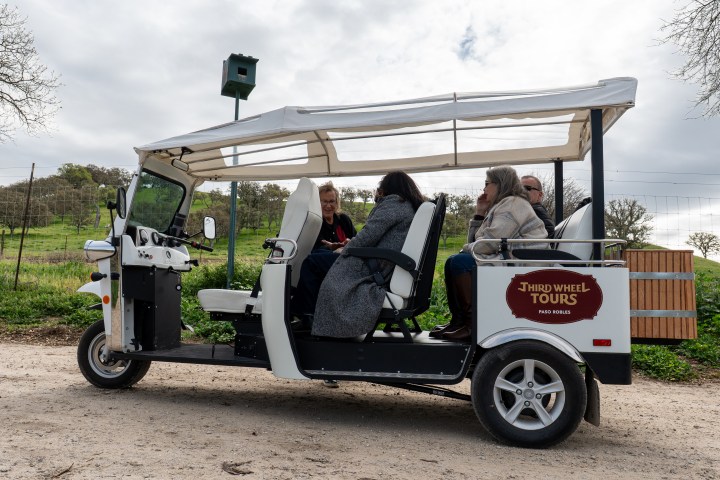 Four people seated in a white open-air tour vehicle on a rural road.
