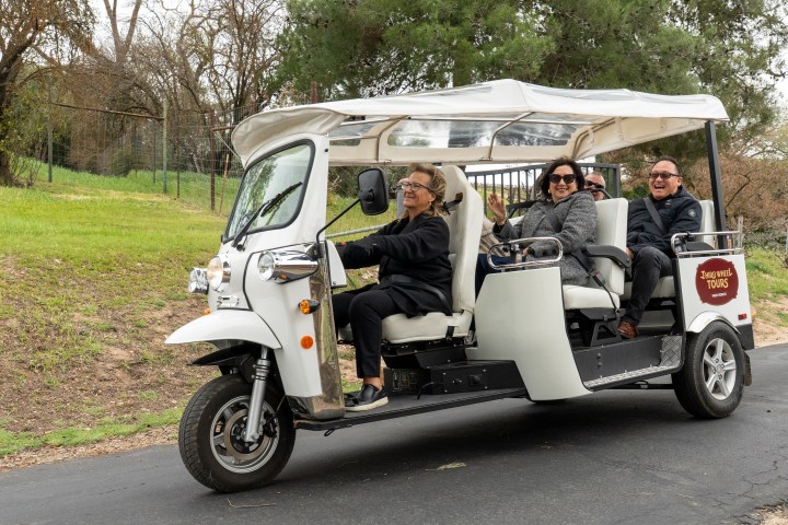 Tourist group enjoying a ride in a three-wheeled tour vehicle on a paved road.