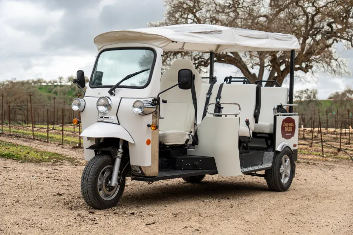 White three-wheeled vehicle with canopy parked on dirt road.