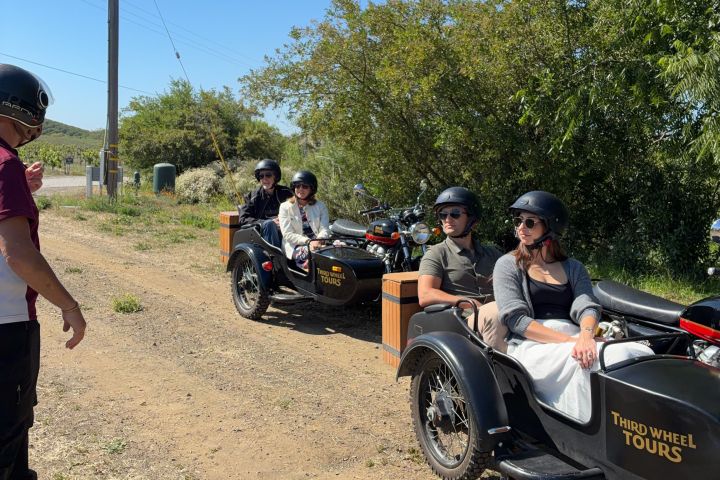 People on sidecar motorcycles parked on a dirt road with trees.