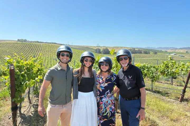 Group of four people wearing helmets in a vineyard under a clear blue sky.