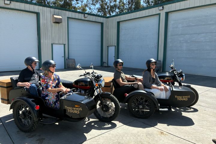 Two motorcycle sidecars with passengers parked by industrial garage doors.