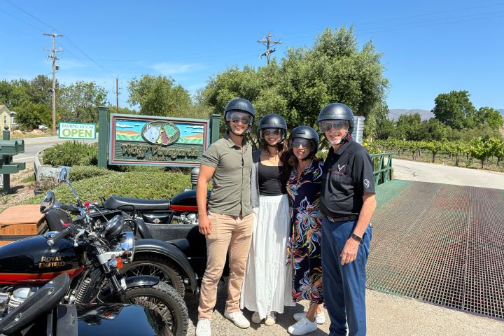 Four people in helmets posing by motorcycles near a vineyard sign.